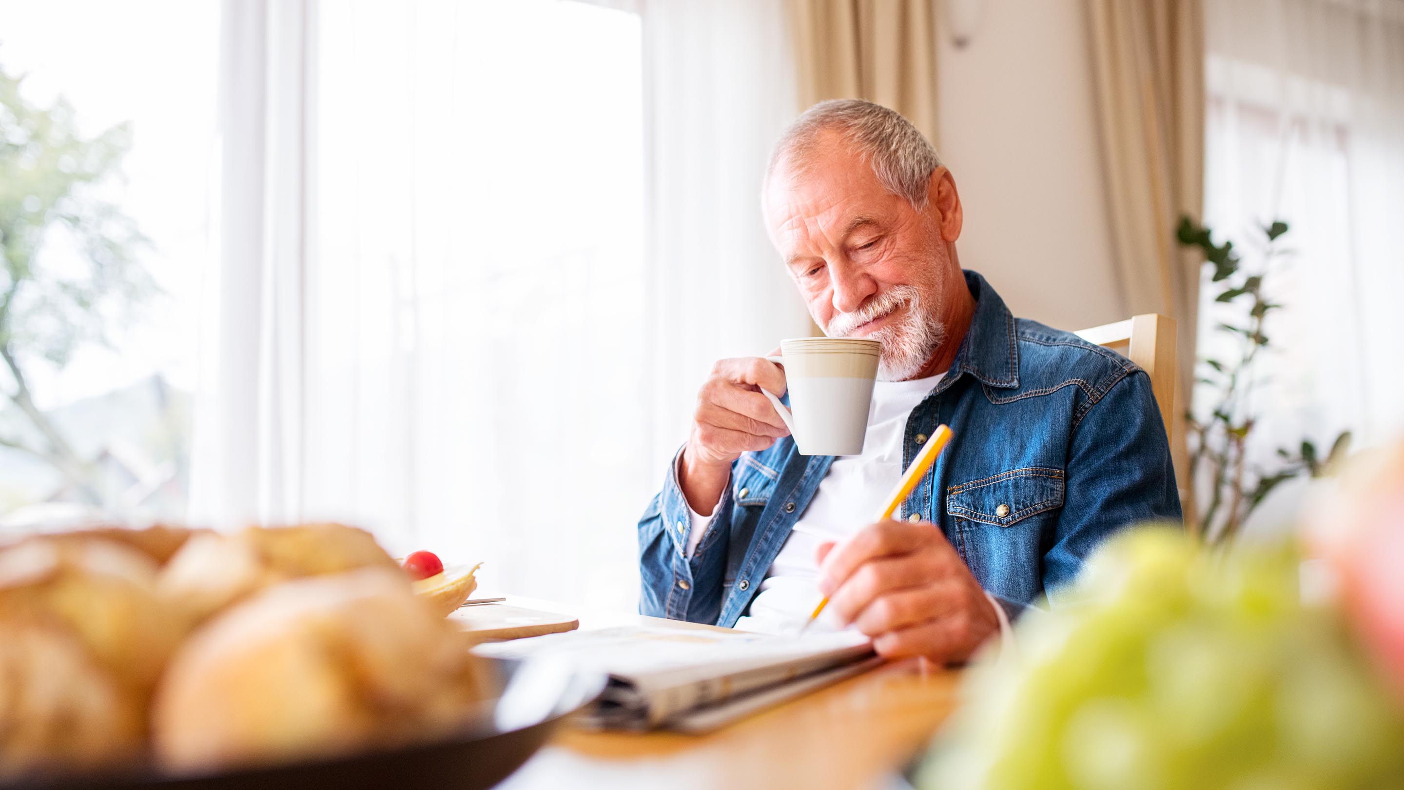 Smiling man sitting at a table, drinking from a mug while writing on paper